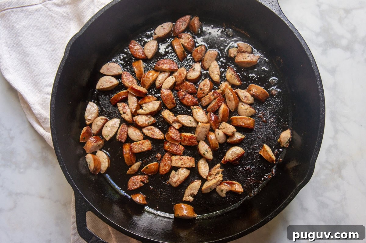 Sausage and Pepper Pasta Recipe — Quick Weeknight Dinner 4 a cast iron skillet with sausage browning in it.