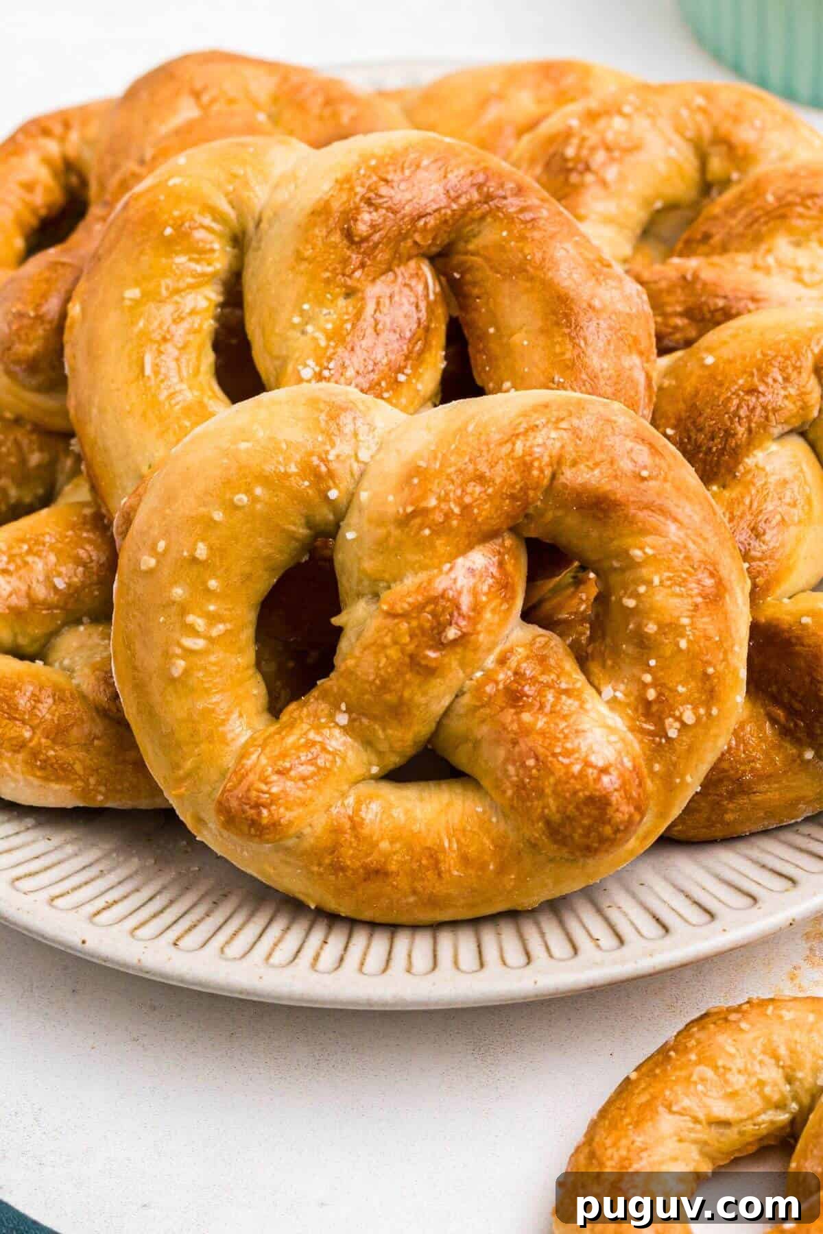 Crispy-On-The-Outside, Soft-On-The-Inside Air Fryer Pretzels 2 Golden brown soft pretzels on a round white plate with a bowl of melted cheese on a marble table.