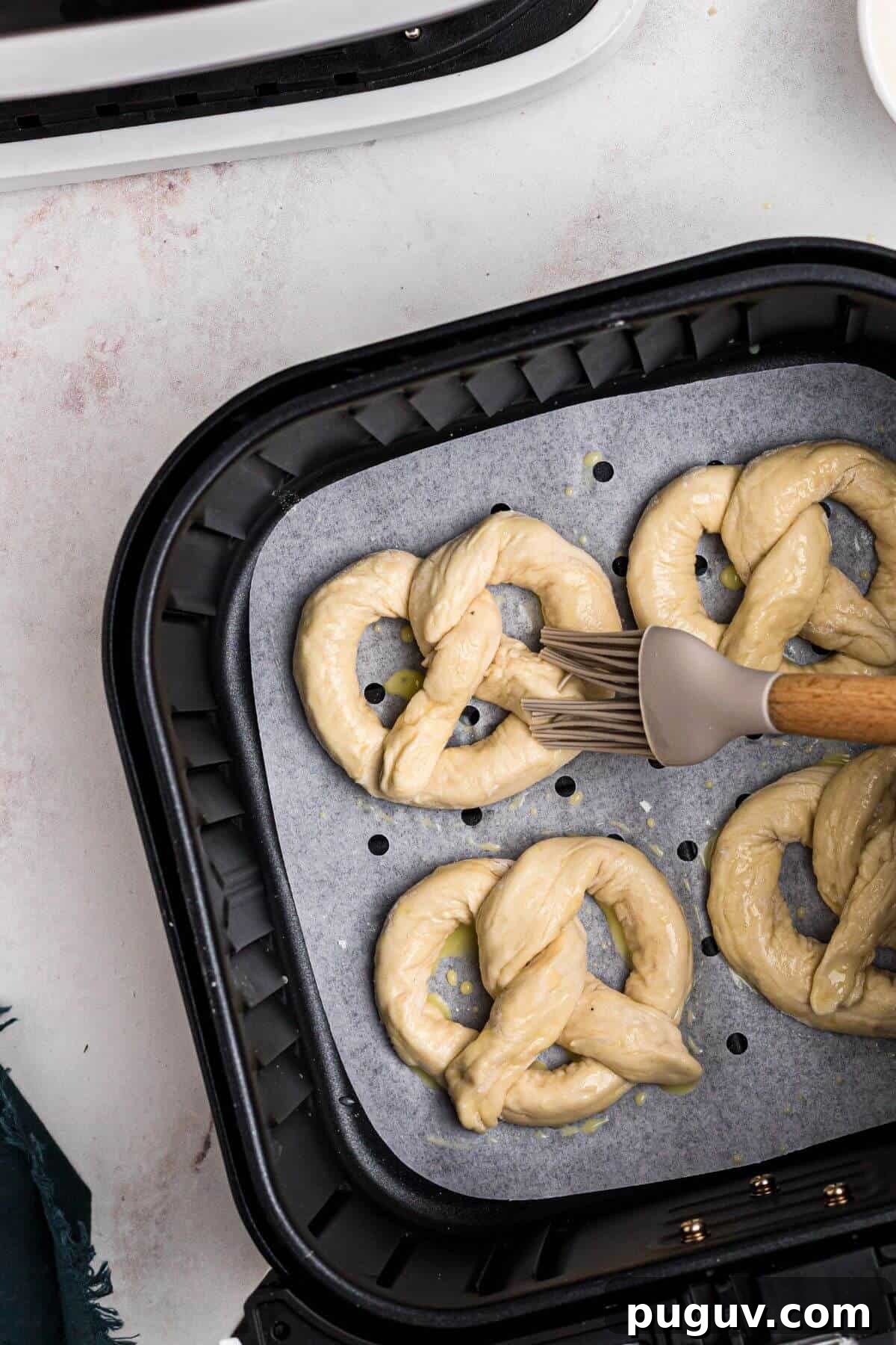 Crispy-On-The-Outside, Soft-On-The-Inside Air Fryer Pretzels 8 Uncooked pretzels in the air fryer basket being brushed with egg wash.