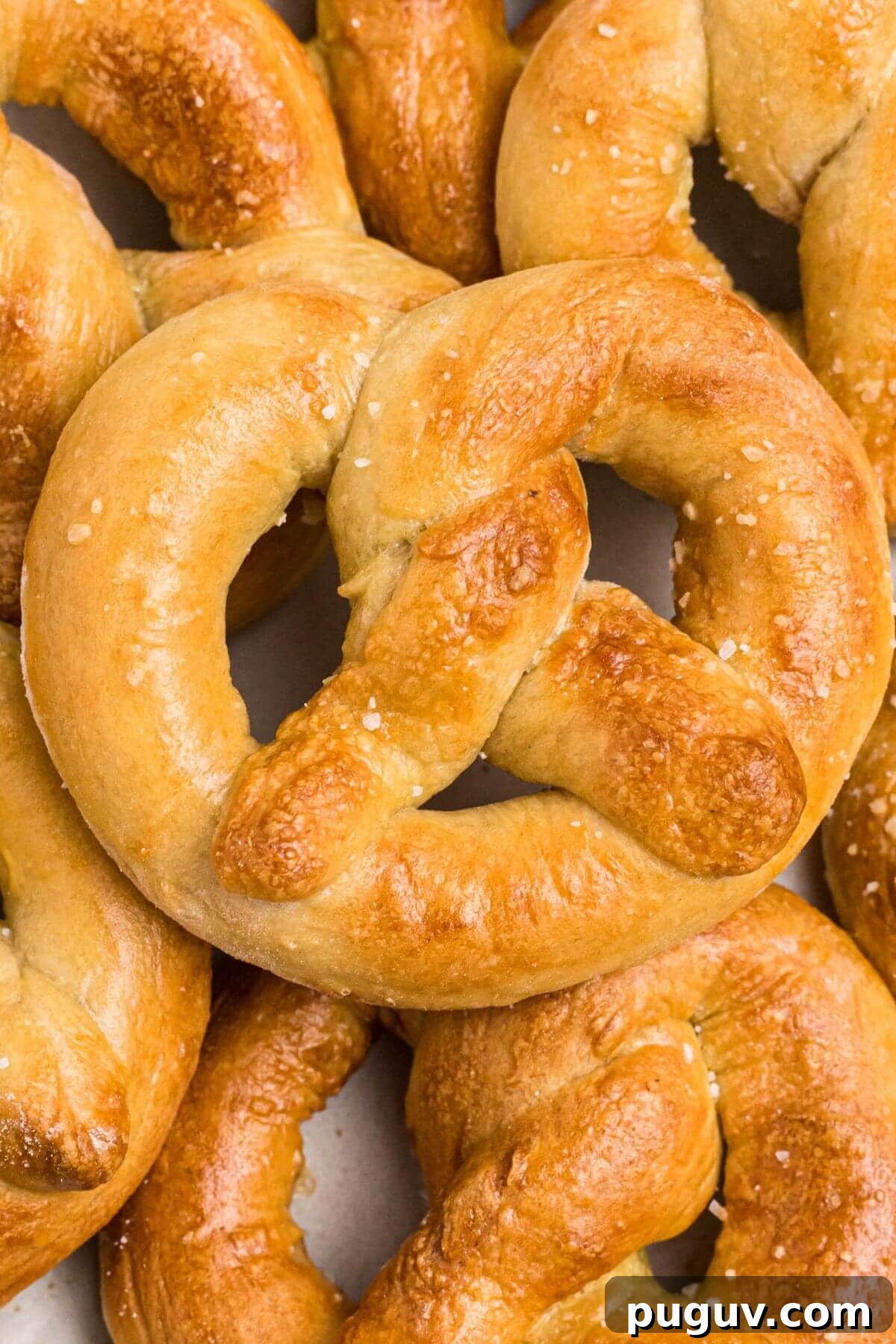 Crispy-On-The-Outside, Soft-On-The-Inside Air Fryer Pretzels 10 Golden soft pretzels stacked on a white plate and sprinkled with coarse salt.