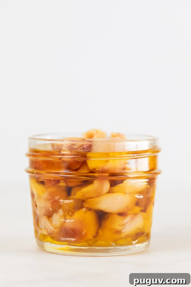 A side shot of a glass jar with roasted garlic cloves and covered with oil