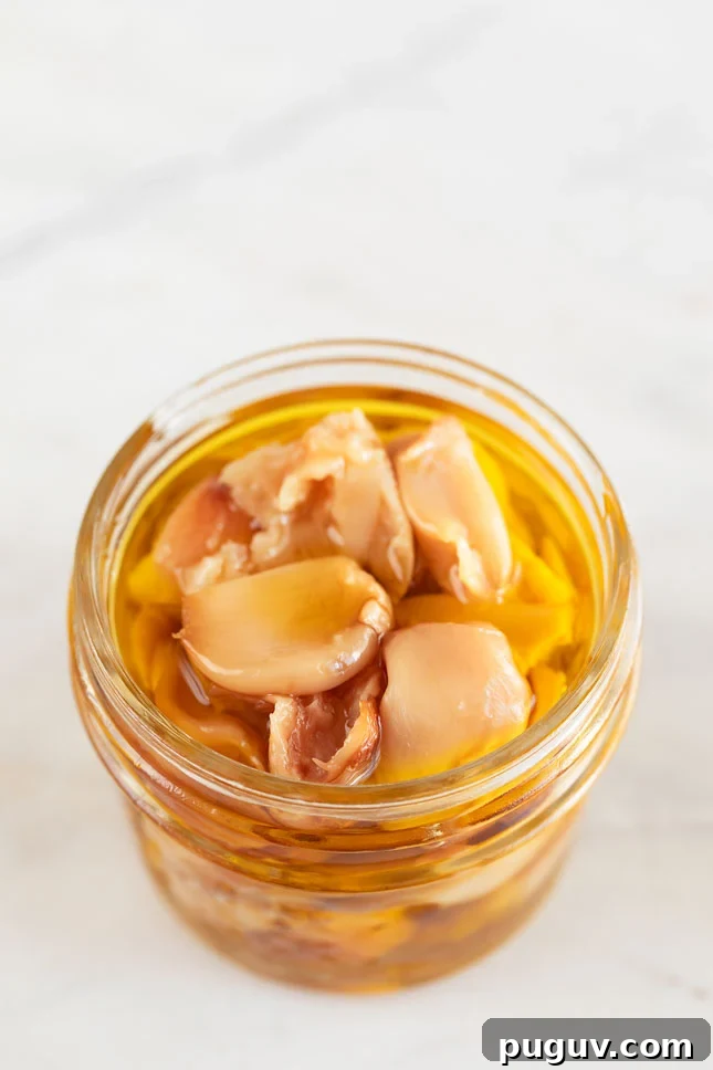 A small glass container with roasted garlic cloves and covered with extra virgin olive oil