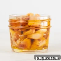 A small picture of a glass container with roasted garlic and covered with oil