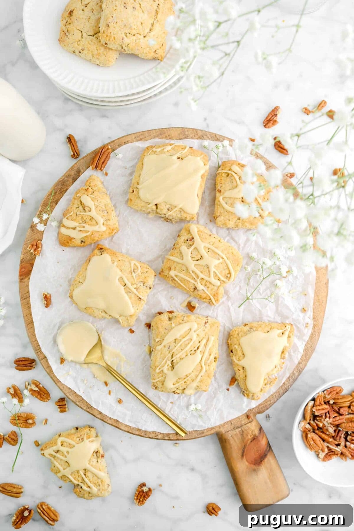 Maple Pecan Scones with Sweet Maple Glaze 4 scones on wood serving board with flowers above, a gold spoon with icing and whole pecans scattered around