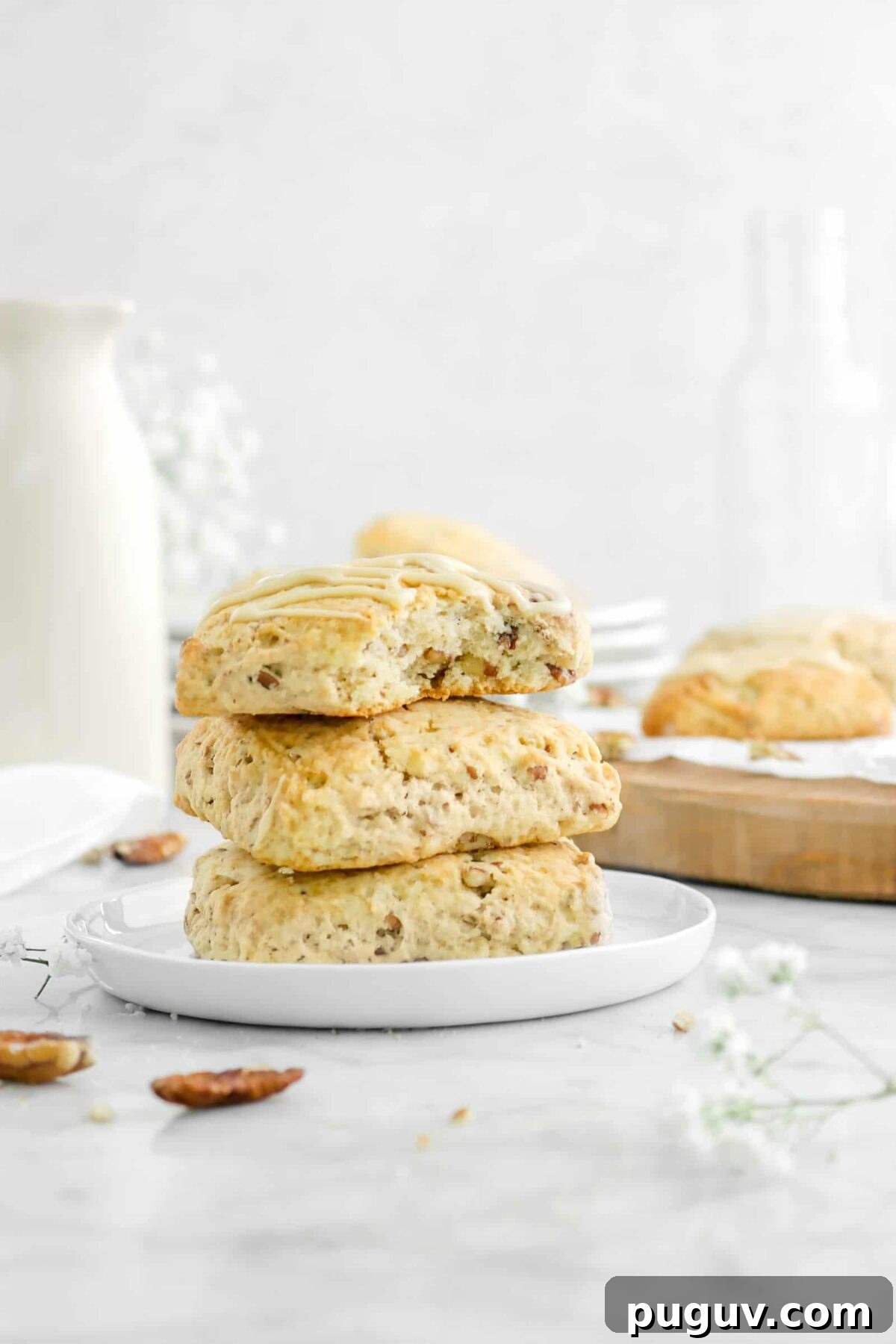 Maple Pecan Scones with Sweet Maple Glaze 5 three stacked scones on white plate with a bite missing and flowers around