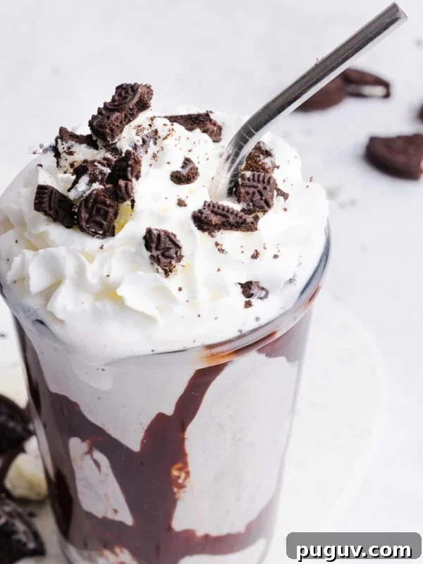 Ninja Creami Oreo Milkshake in a glass with whipped cream, crushed Oreos and chocolate sauce.