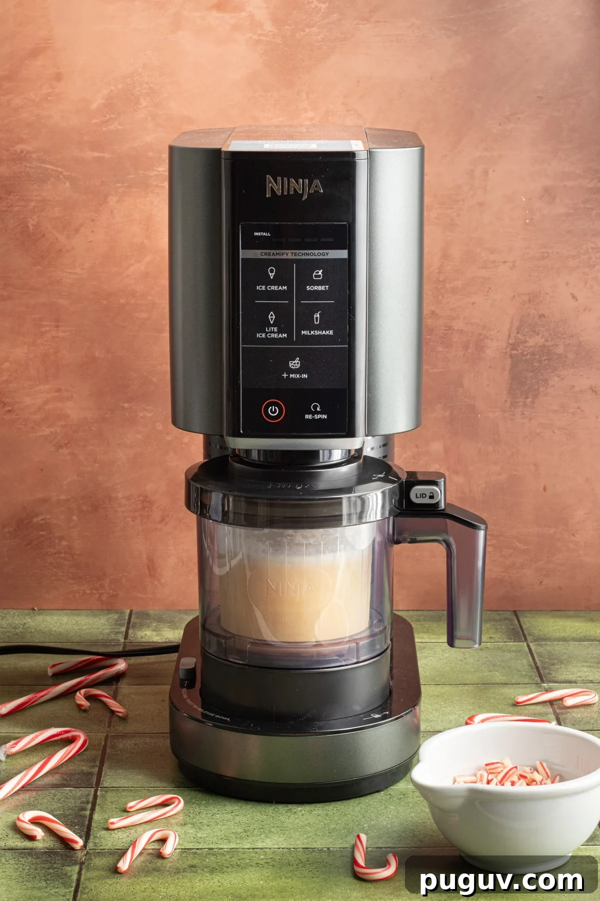 Ninja Creami ice cream machine with bowl attached to frozen peppermint ice cream base on a green counter top.