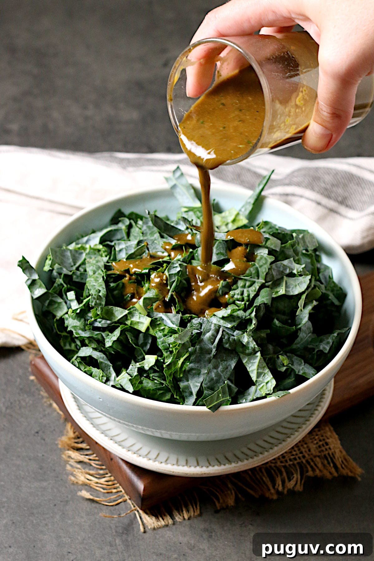 Basil Balsamic Vinaigrette Recipe — Tangy Herb Dressing for Salads 5 A hand pouring Basil Balsamic Vinaigrette onto a bowl of shredded kale.
