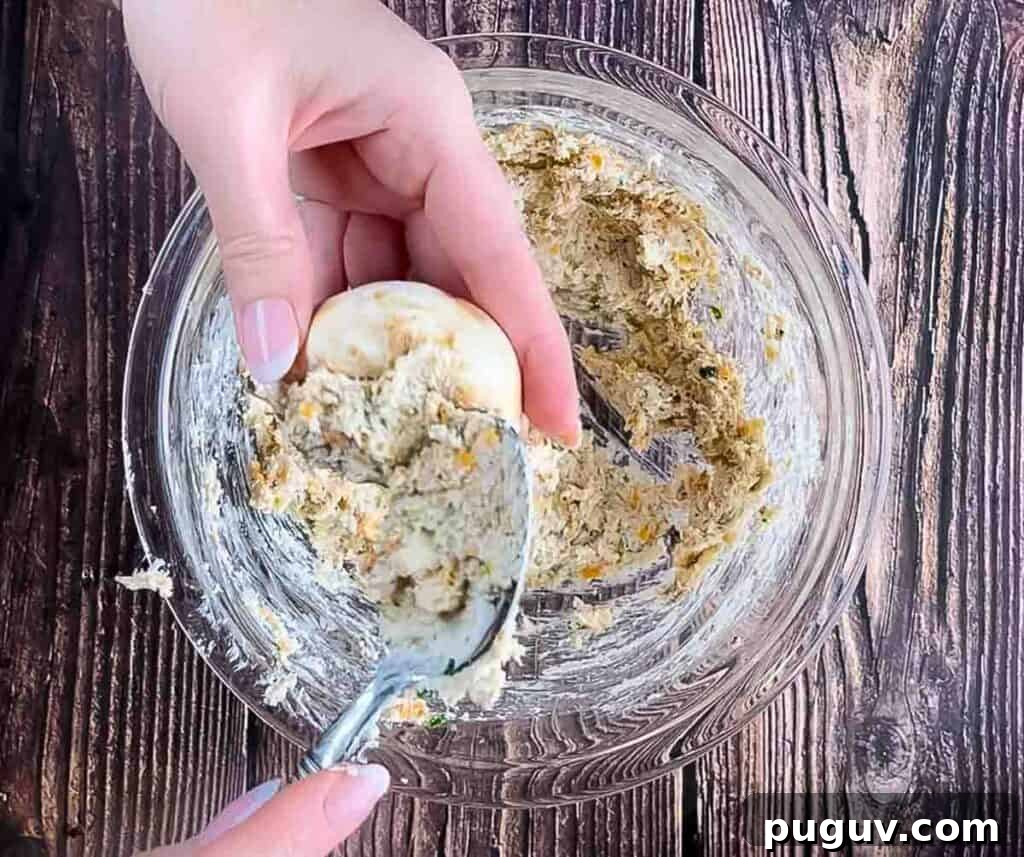A hand using a spoon to stuff the stuffing mixture into the mushroom caps.