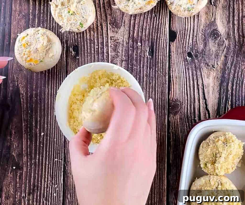 A hand putting the mushroom into the breadcrumb mixture.