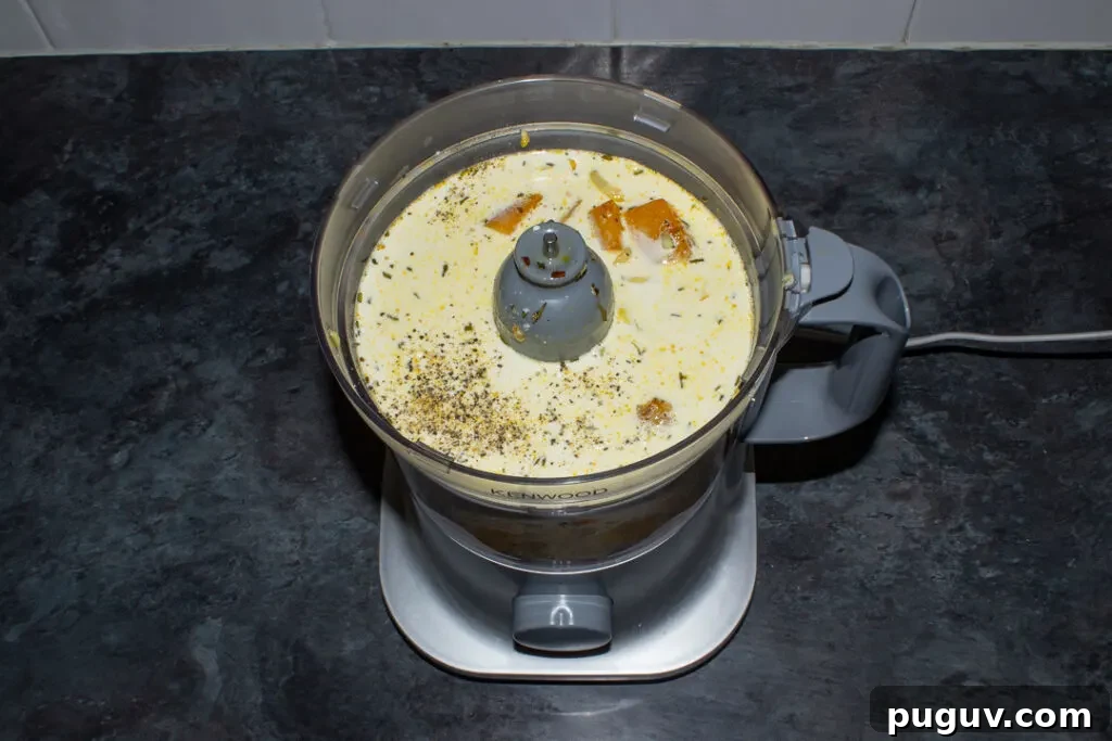 Spicy roast butternut squash ingredients in a blender set on a kitchen worktop.
