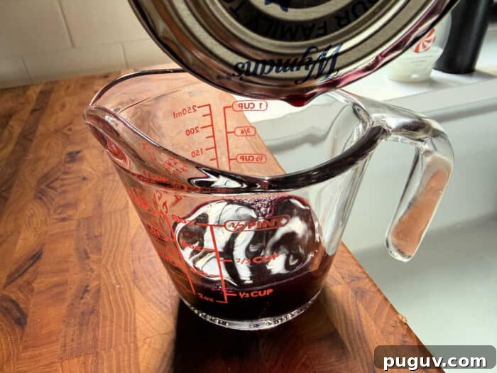 Upgrade Your Blueberry Muffin Mix: Simple Tips for Moist, Flavorful Muffins 4 Red liquid being poured from a can into a glass measuring cup on a wooden countertop—perfect for learning how to make blueberry muffin mix better with flavorful additions.