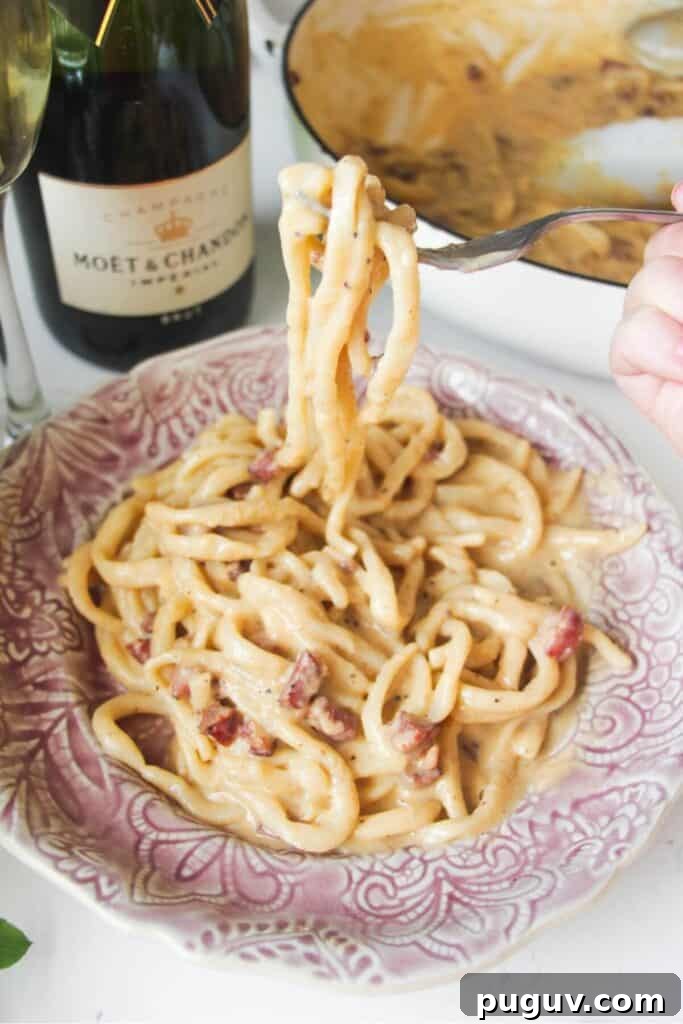 Spicy ’Nduja Pasta with Creamy Burrata Cheese 14 Fork holding up strands of aspaghetti, with a plate of carbonara in the foreground.