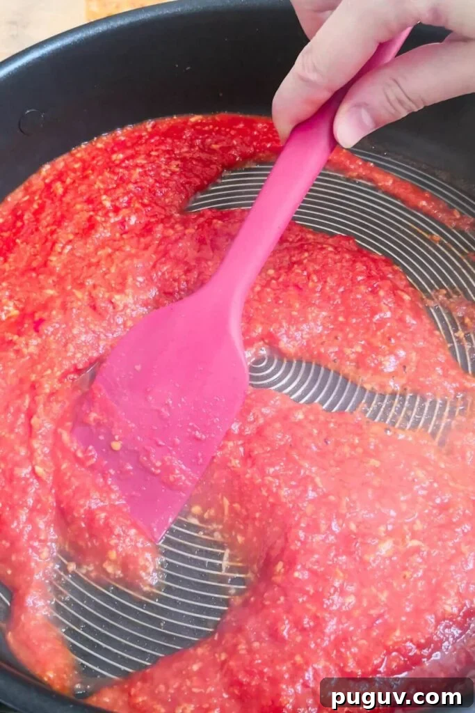 Spicy ’Nduja Pasta with Creamy Burrata Cheese 5 Red spatula stirring nduja tomato sauce in a large black pan.