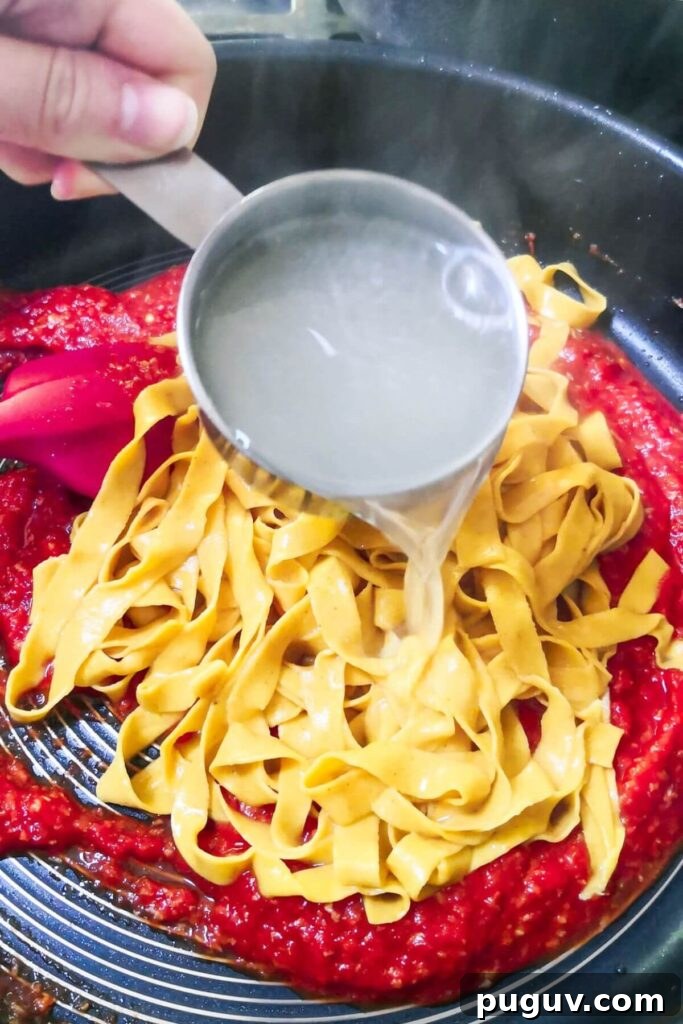 Spicy ’Nduja Pasta with Creamy Burrata Cheese 6 A small cup of pasta water being added to pasta and nduja pasta sauce in a large pan.