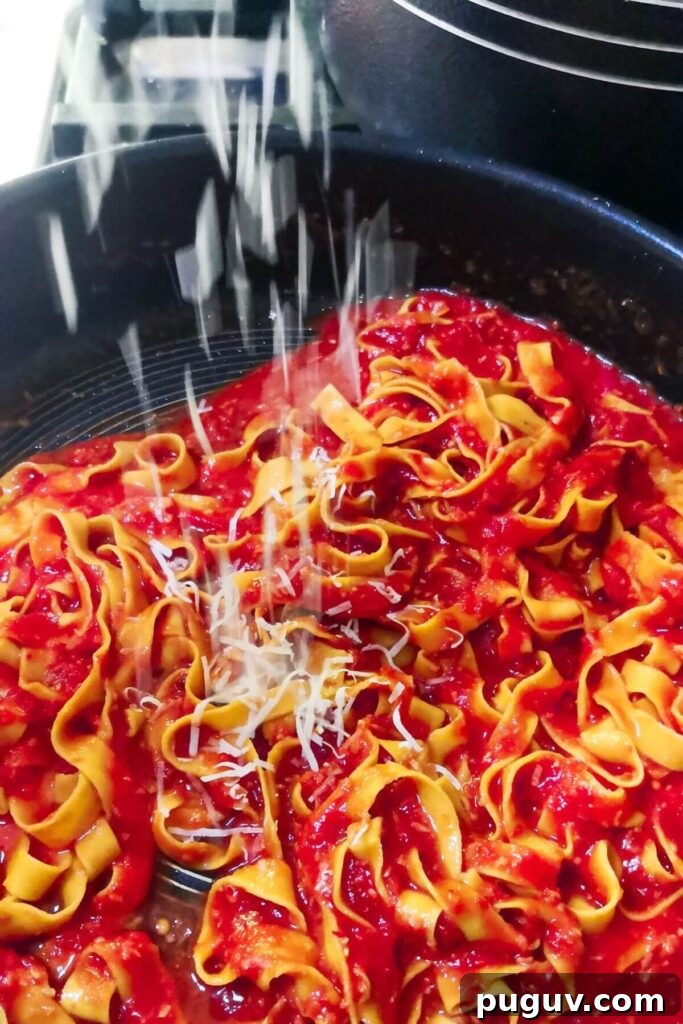 Spicy ’Nduja Pasta with Creamy Burrata Cheese 7 Grated parmesan being scattered on top of nduja pasta in a large pan.