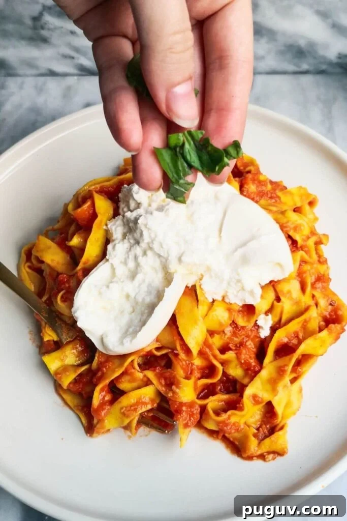 Spicy ’Nduja Pasta with Creamy Burrata Cheese 9 A hand adding basil to burrata on top of nduja pasta on a large white plate.