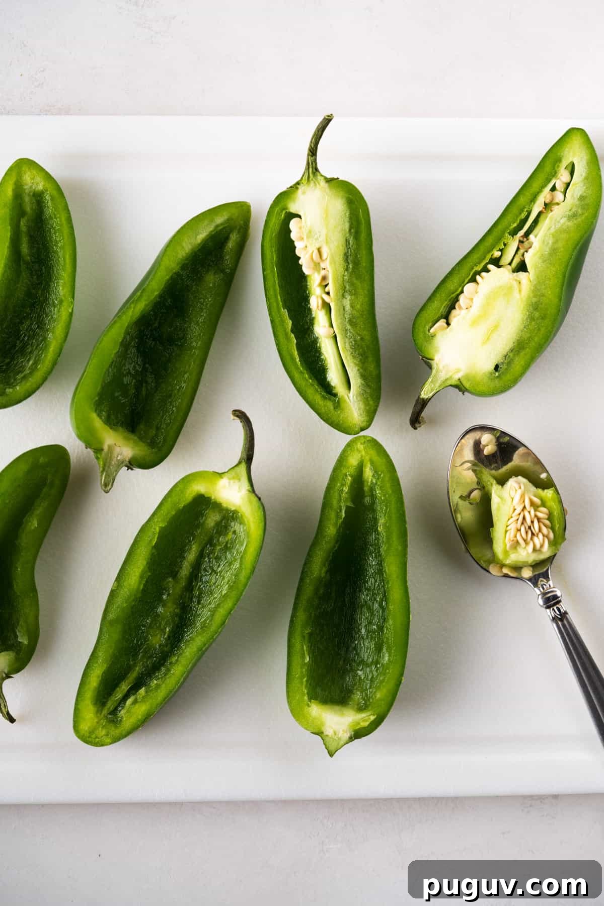 Crispy Air Fryer Jalapeño Poppers: Cream Cheese Stuffed Bites 3 Jalapeños sliced lengthwise on a cutting board and a spoon hallowing out the some of the jalapeños