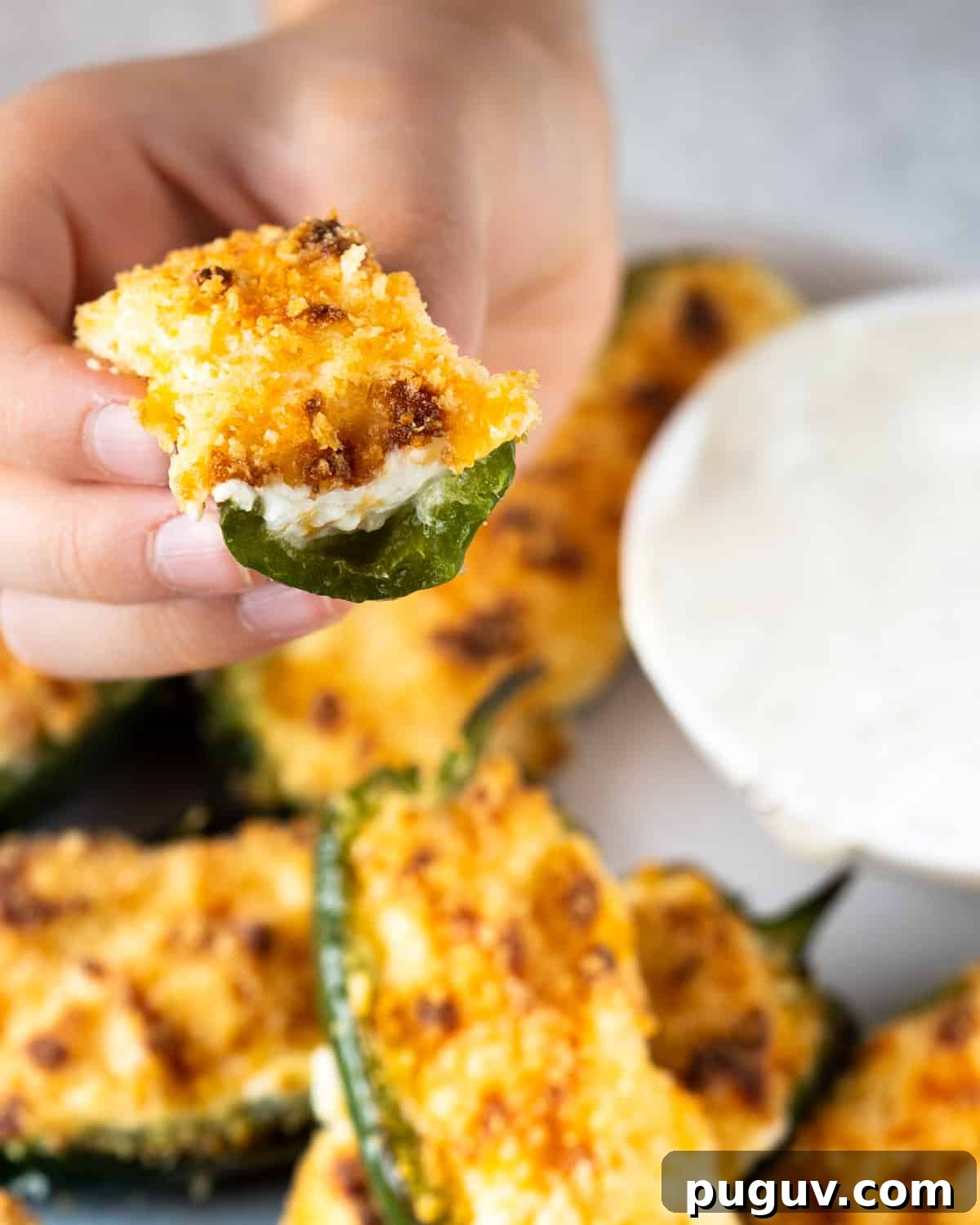 Crispy Air Fryer Jalapeño Poppers: Cream Cheese Stuffed Bites 7 plate of jalapeño poppers in the background and a hand holding up a bitten jalapeño popper to show the inside
