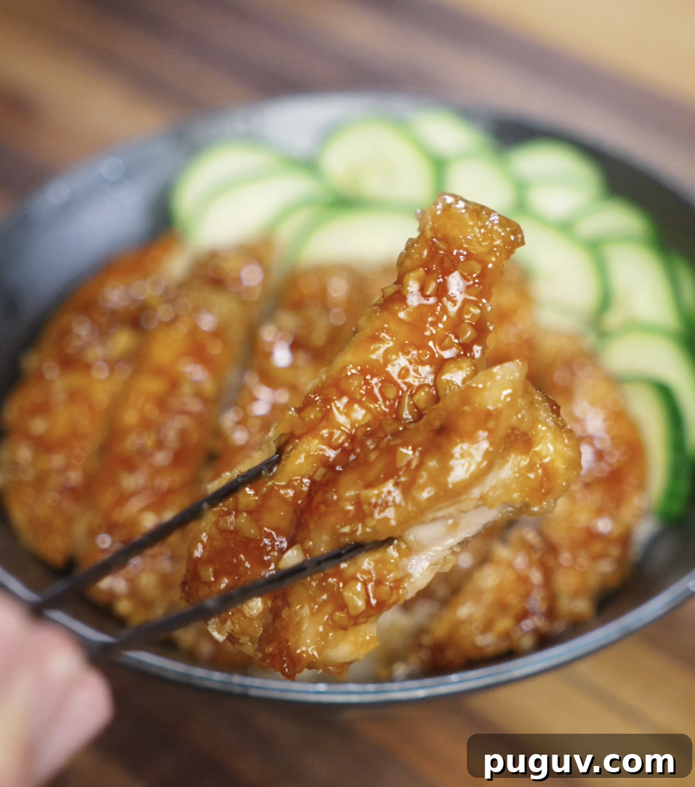 Crispy Honey Garlic Chicken Recipe — Sticky Glazed Chicken Drumsticks 3 A piece of crispy chicken coated in honey garlic glaze is held up with chopsticks, highlighting the juicy interior and glossy, crunchy exterior.