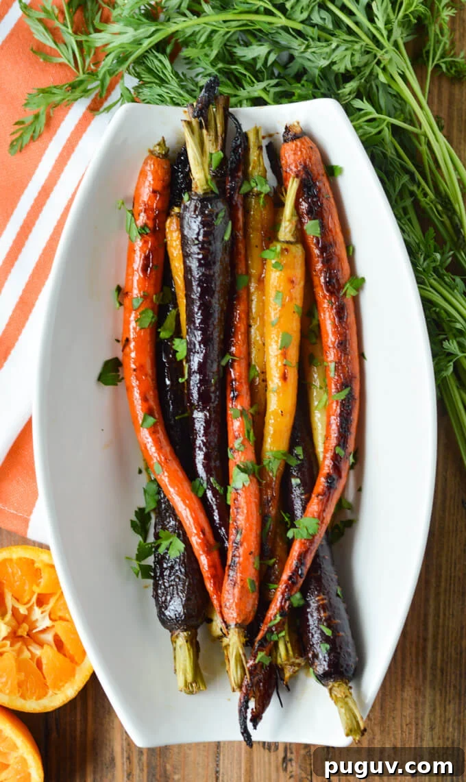 A white serving bowl of candied rainbow carrots with a orange and white napkin, parsley and a half squeezed half orange next to the bowl.