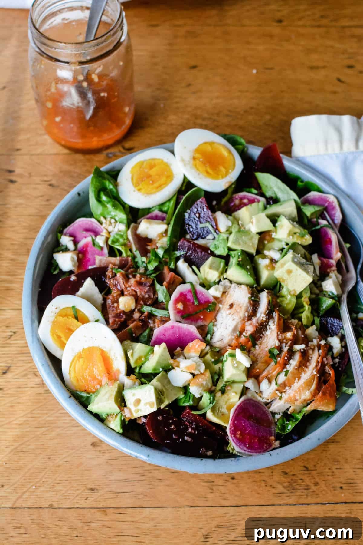 Autumn Harvest Cobb Salad with Cranberries, Apples & Goat Cheese 4 An overhead image of a large salad sitting on a wooden table with a fork in it and a jar of homemade dressing near by.