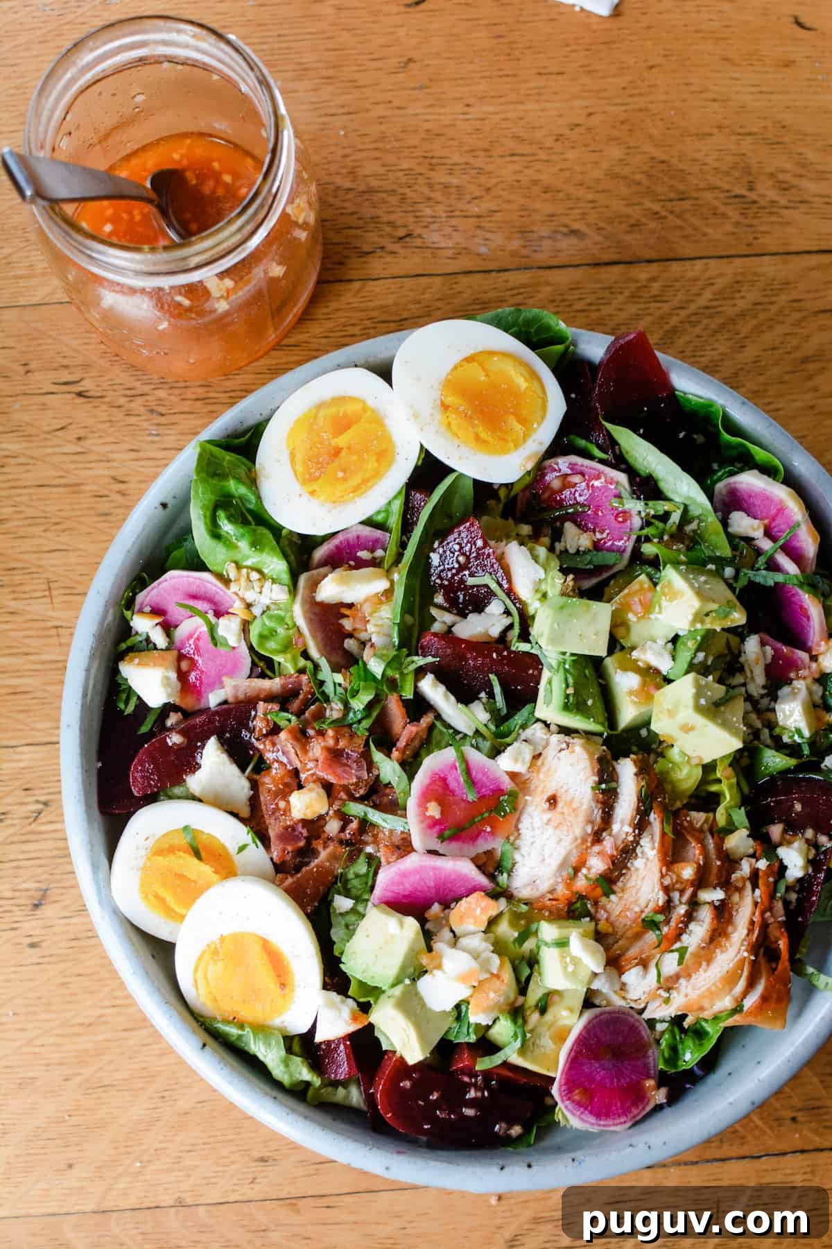 An overhead image of a large salad sitting on a wooden table with a jar of salad dressing sitting near by.