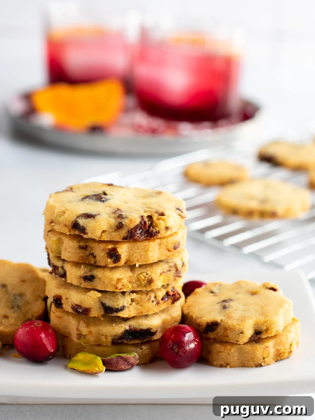 Cranberry orange shortbread cookies on a white plate with the cooling rack and two cocktails in the background.
