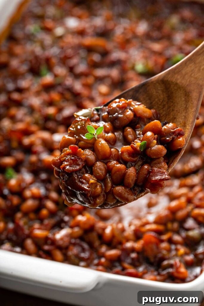 Classic Homemade Baked Beans Recipe for Oven-Baked Flavor 2 Serving baked beans with a wooden spoon from a baking dish