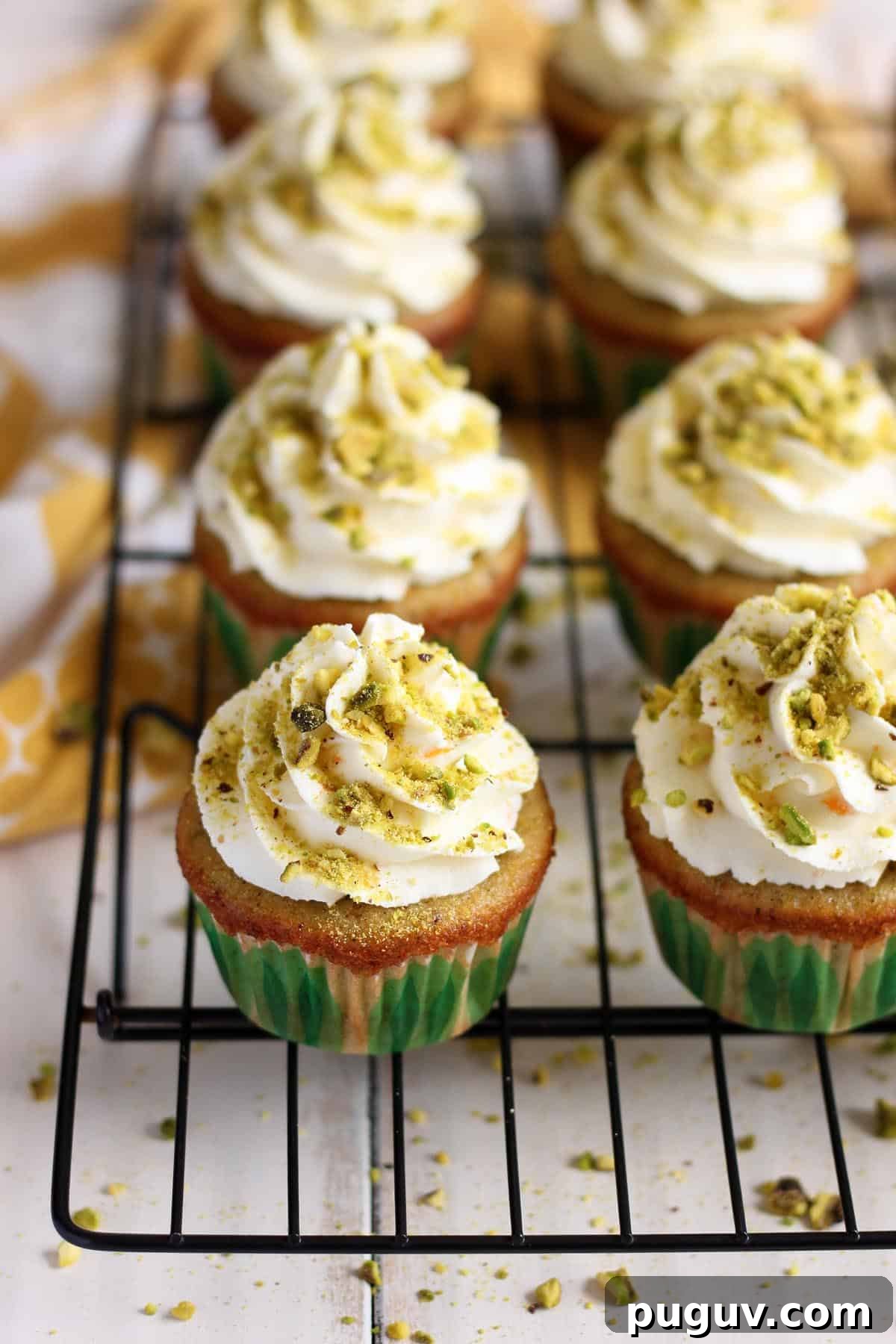 Three quarters view of pistachio cupcakes with orange mascarpone frosting on a wire rack.