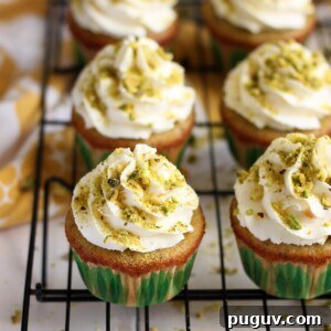 Three quarters view of pistachio cupcakes with orange mascarpone frosting on a wire rack.