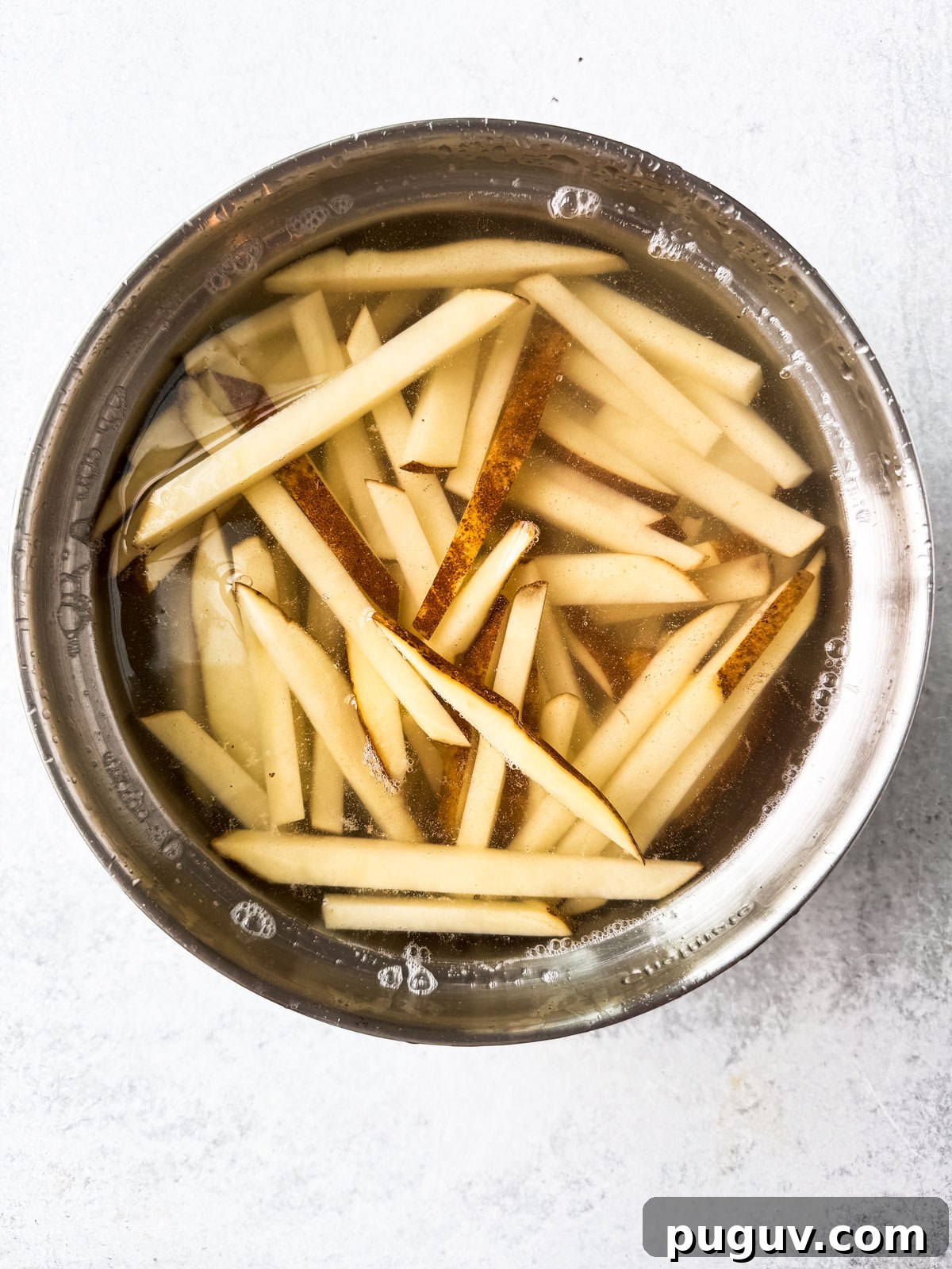 Crispy Air Fryer French Fries with 3 Ingredients 7 Uncooked fries soaking in a bowl of water.