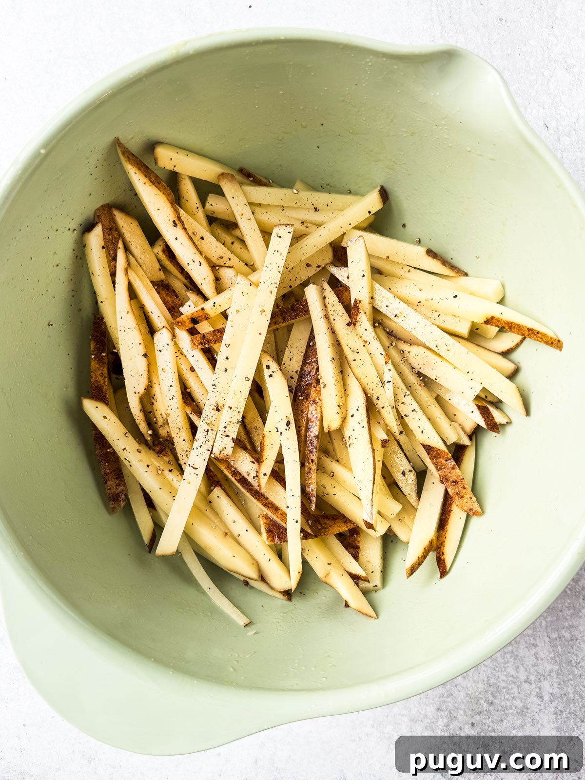 Crispy Air Fryer French Fries with 3 Ingredients 9 Uncooked fries in a mixing bowls with oil and seasoning.