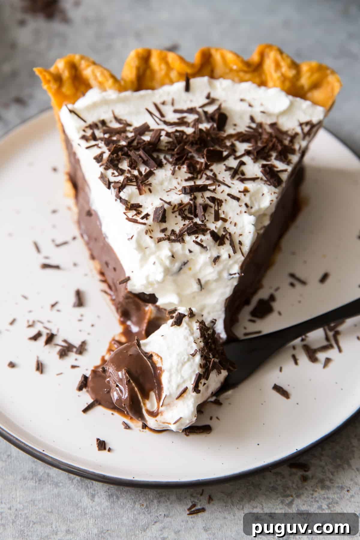 A fork pulls away a bite from a slice of pie on a plate.