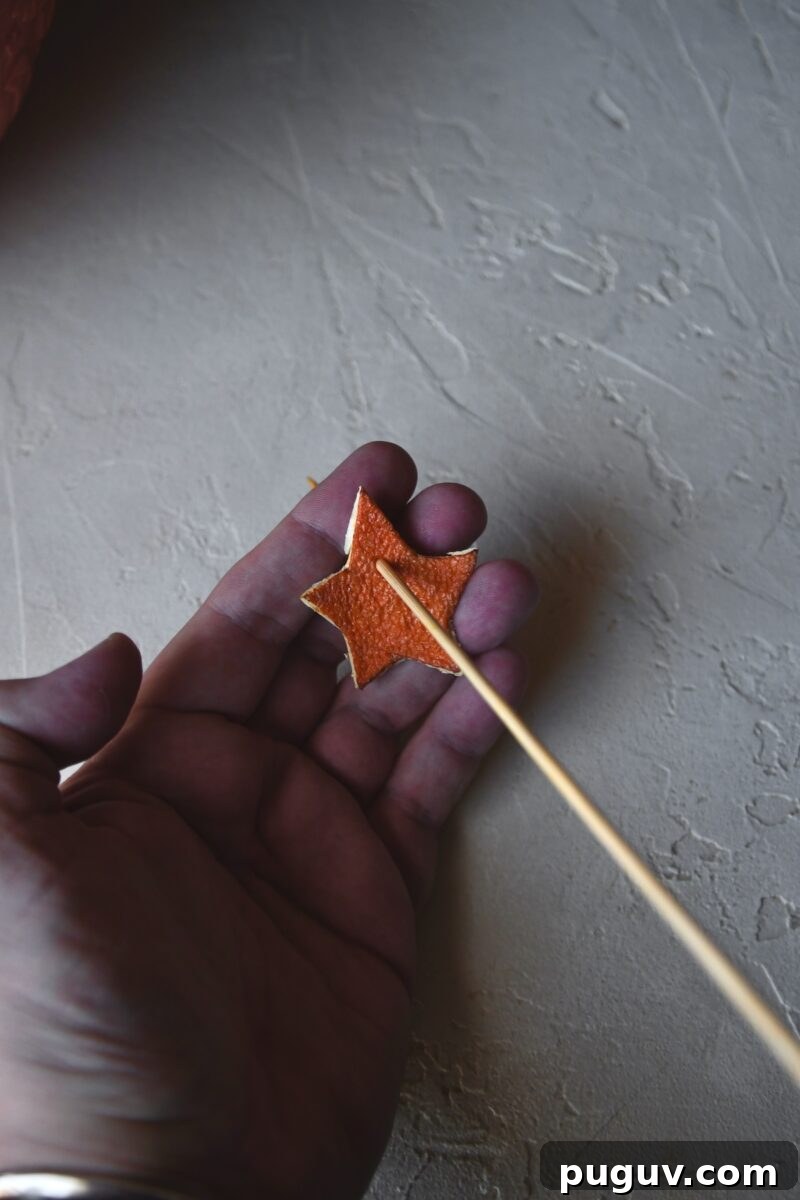 DIY Orange Peel Star Garland: Natural Holiday Decoration Tutorial 11 Using a skewer to poke a hole in dried orange peel stars.