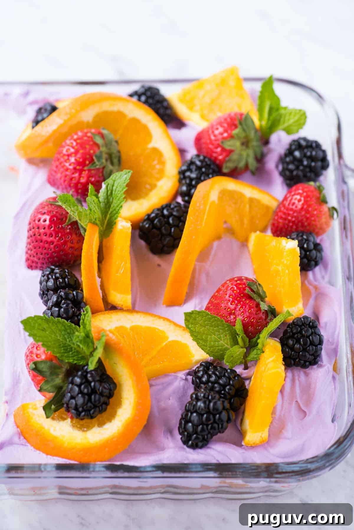 Sangria-Inspired Poke Cake Recipe for Summer Parties 2 sangria poke cake decorated with orange slices, strawberries, blackberries and mint leaves in a glass pan