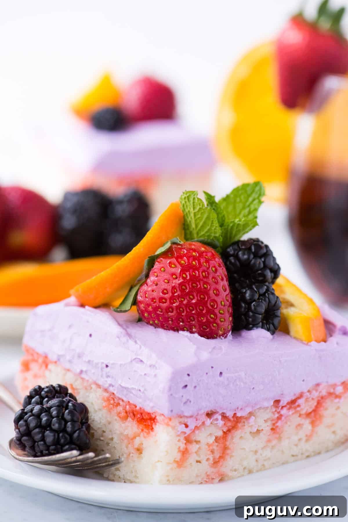 Sangria-Inspired Poke Cake Recipe for Summer Parties 4 slice of sangria poke cake garnished with a strawberry, blackberries, orange slice and mint leaf on white plate