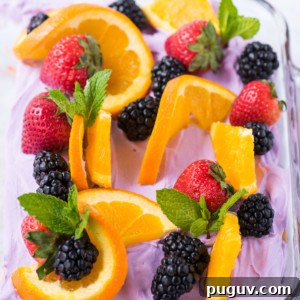 Sangria-Inspired Poke Cake Recipe for Summer Parties 6 A glass dish filled with purple whipped topping, garnished with fresh orange slices, whole strawberries, blackberries, and sprigs of mint—perfect for dressing up a sangria poke cake.