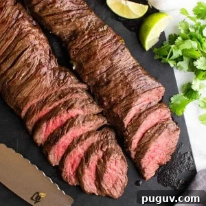 sliced carne asada made in the oven on a black cutting board with knife and citrus fruits photographed from above.
