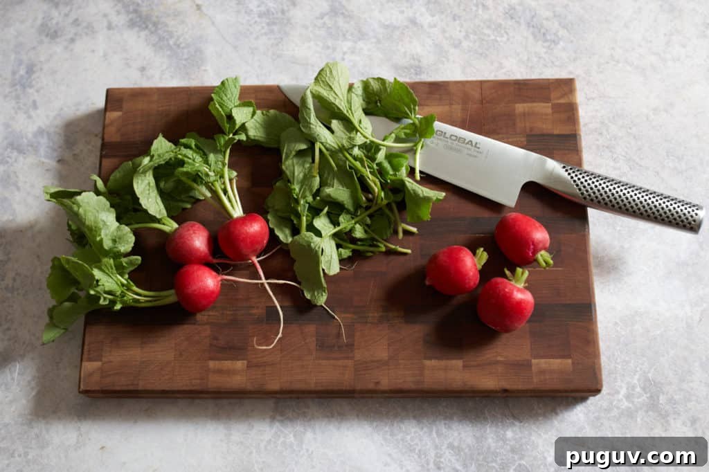 Radishes being trimmed of their leaves on a cutting board with a knife.