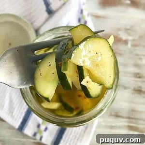 Quick Refrigerator Pickled Cucumbers: Tangy Crunch in 24 Hours 7 Close up of silver fork wit pickled cucumbers from a jar. White blue kitchen towel beneath on a washed white table.