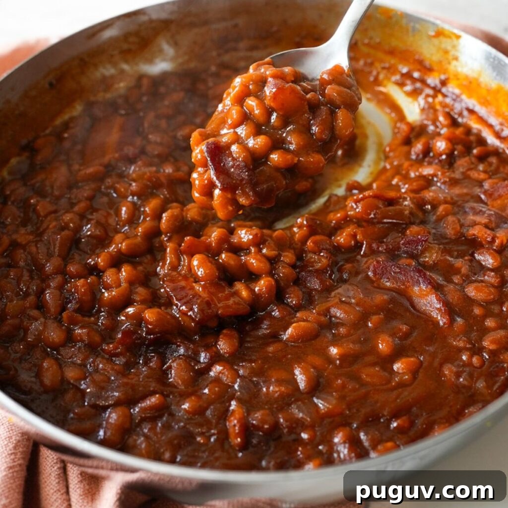 Classic Oven-Baked Beans Recipe with Step-by-Step Video 2 Baked beans with crispy bacon in a skillet, served warm and bubbly straight from the oven.