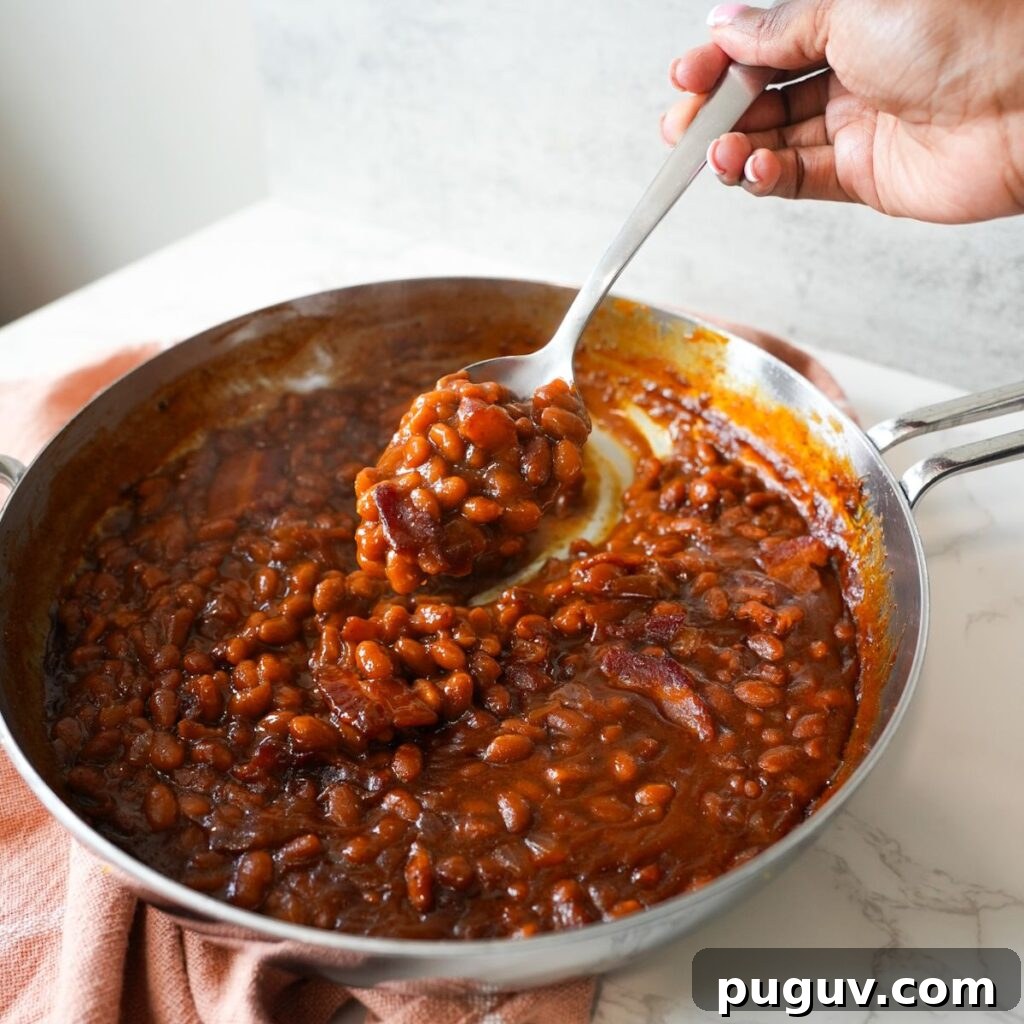 Classic Oven-Baked Beans Recipe with Step-by-Step Video 4 Baked beans with crispy bacon in a skillet, served warm and bubbly straight from the oven.