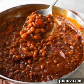 Baked beans with crispy bacon in a skillet, served warm and bubbly straight from the oven.