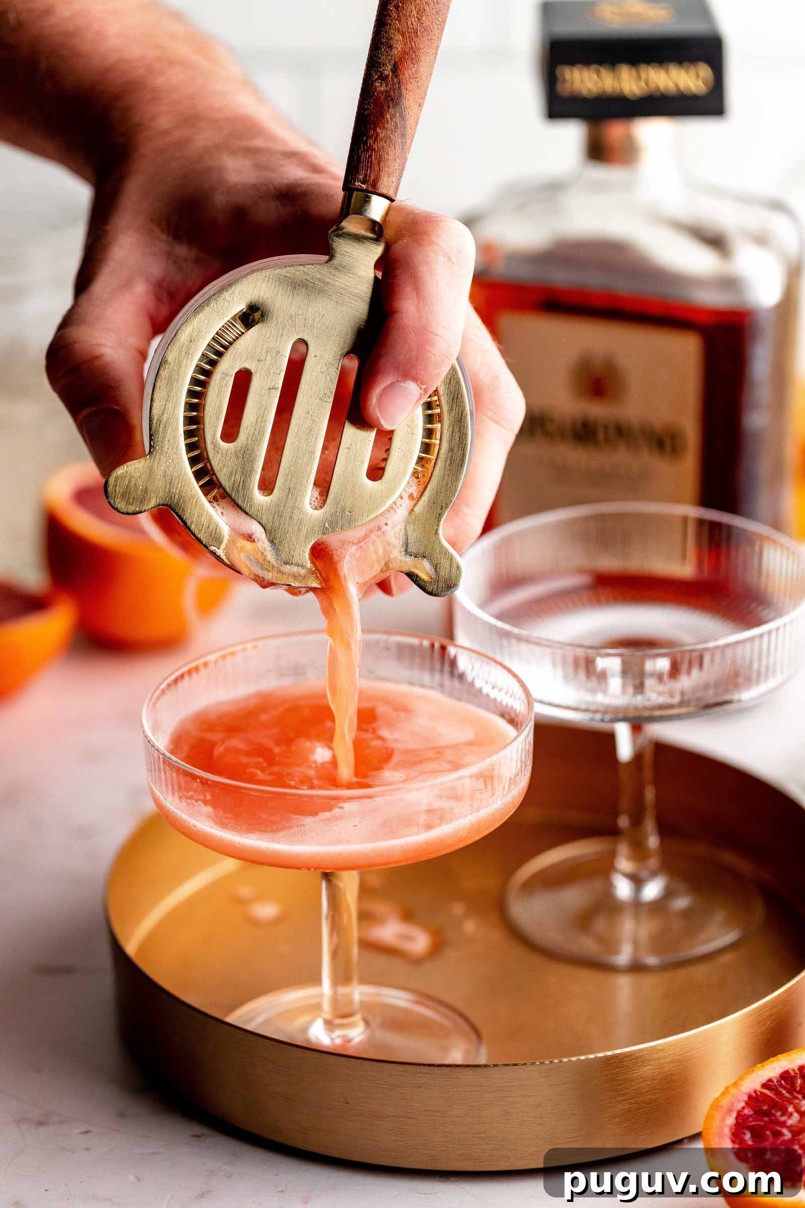 Hand straining cocktail into glass.