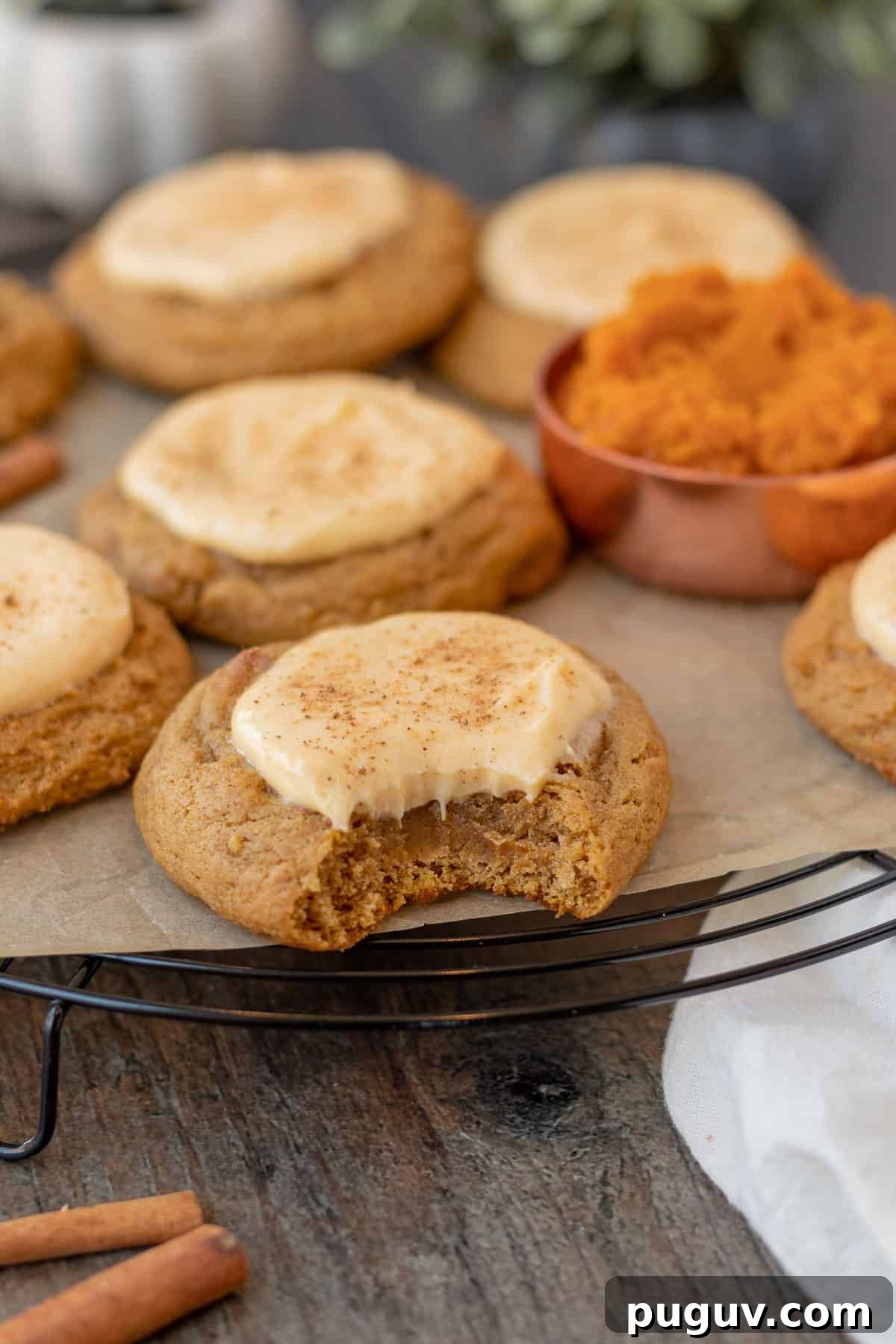 pumpkin cheesecake cookies sitting on a black wire cooling rack with measuring cup of pumpkin next to them