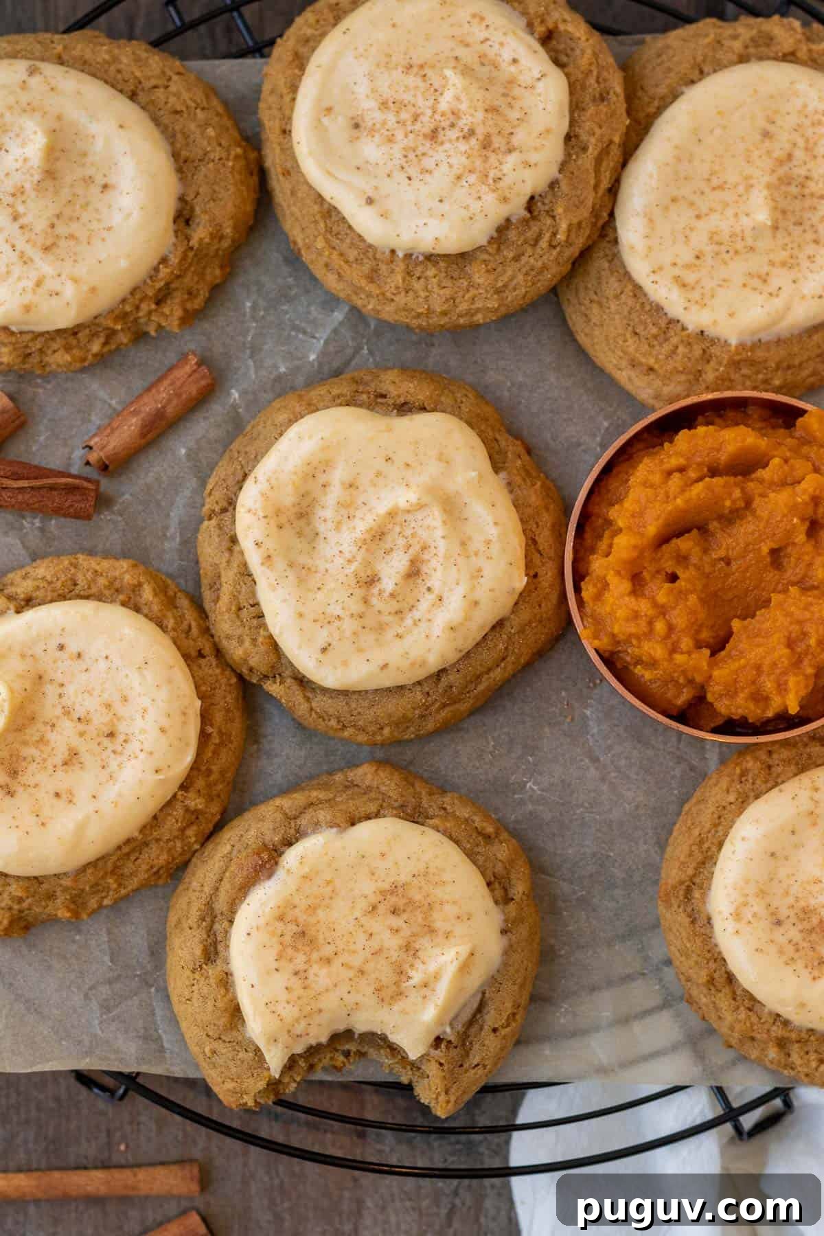 pumpkin cheesecake cookies on a cooling rack on a wood background with pumpkin puree in a measuring cup