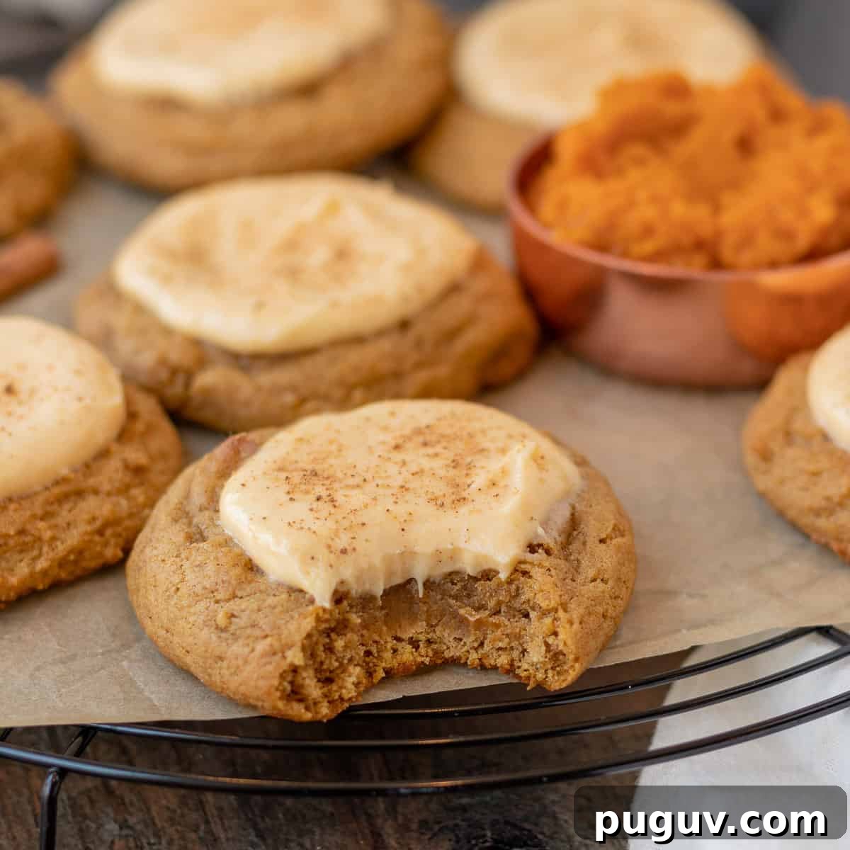 pumpkin cheesecake cookies sitting on a black wire cooling rack with measuring cup of pumpkin next to them