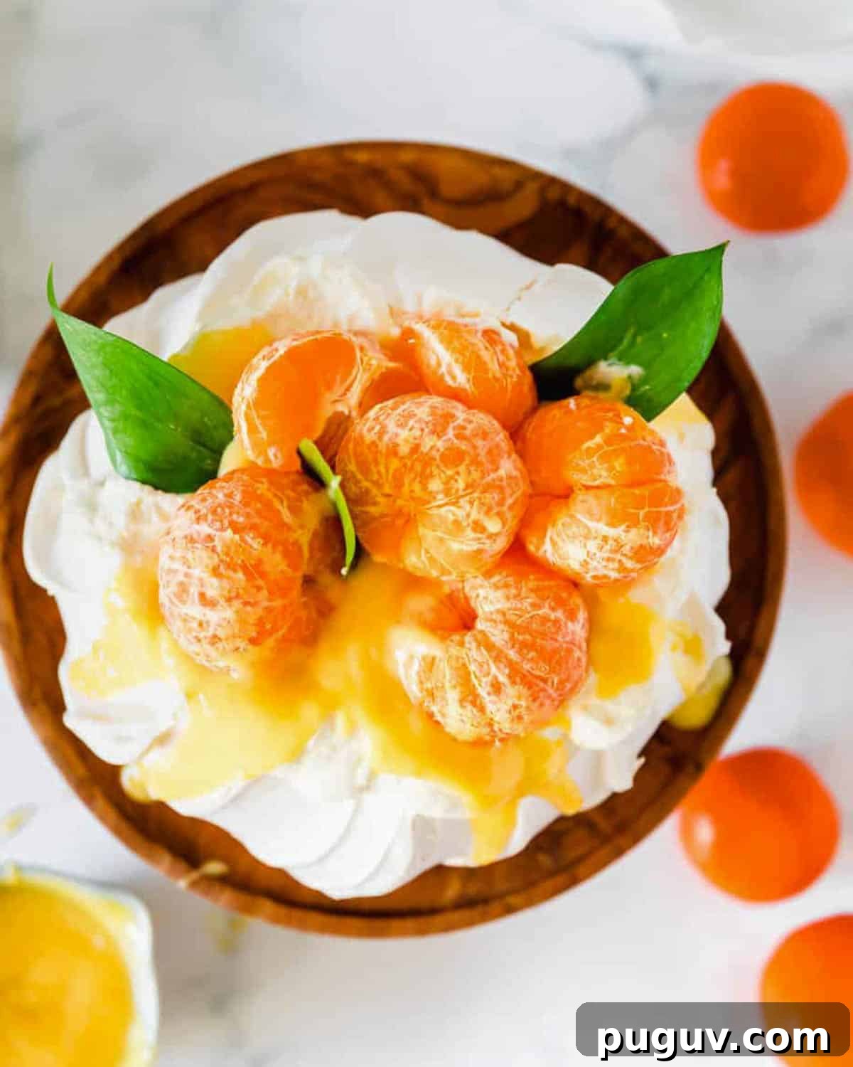 A pavlova topped with clementine curd and fresh fruit sitting on a wooden stand.