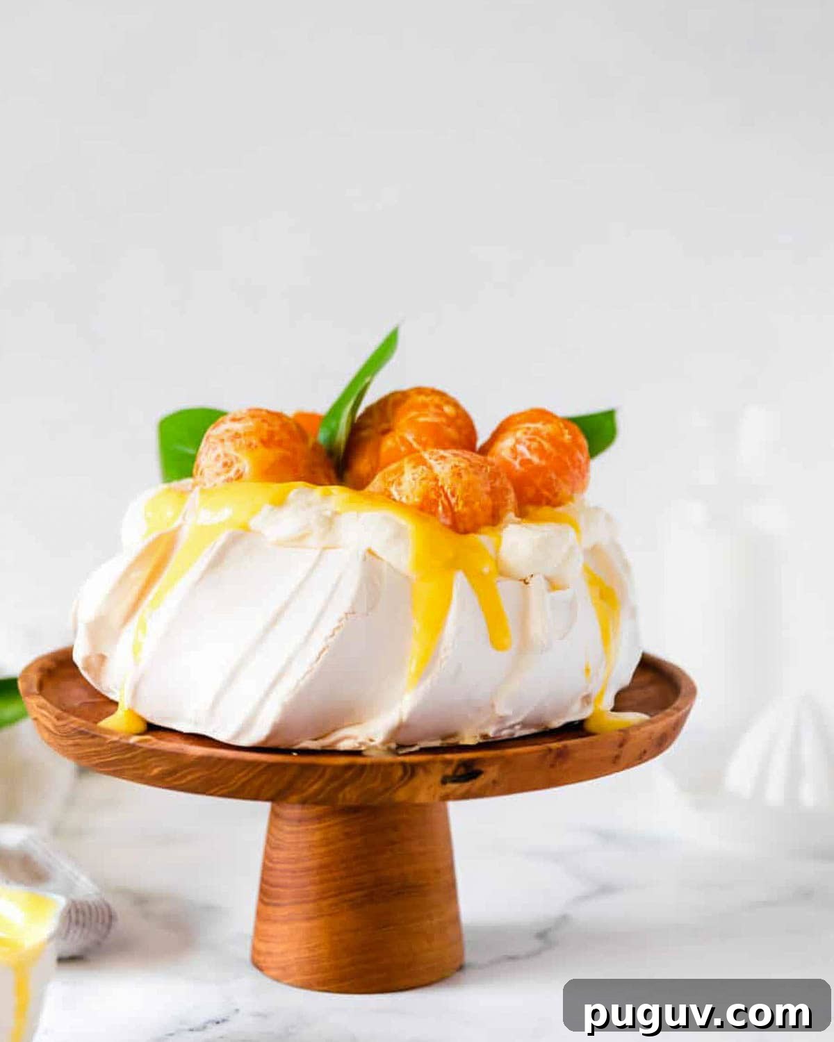 A pavlova served on a wooden cake stand and topped with clementine curd and fresh fruit.